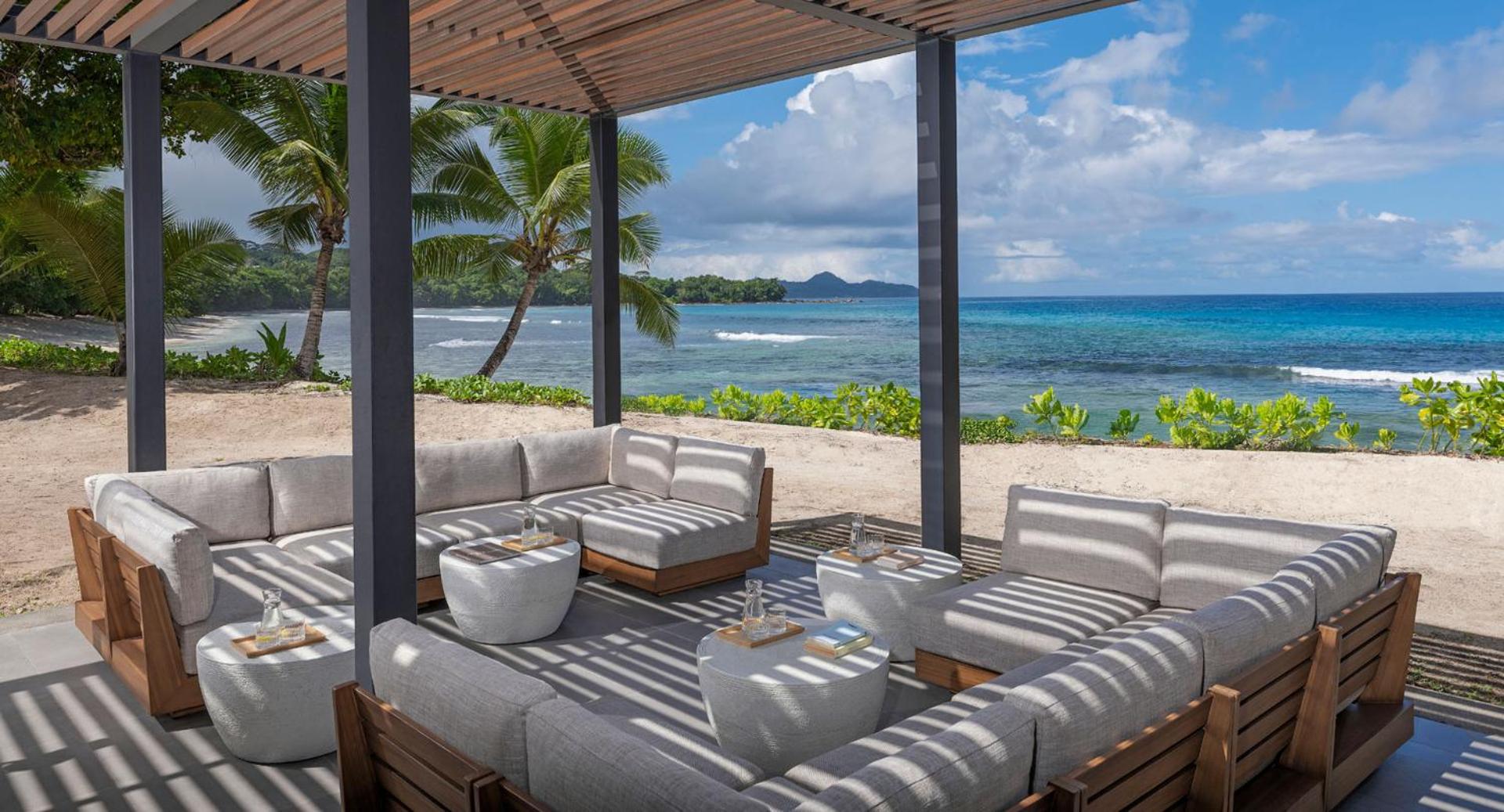 Moderna āra terase ar mīkstajiem dīvāniem zem nojumes Avani+ Barbarons Seychelles viesnīcā — skats uz Indijas okeānu un palmām
