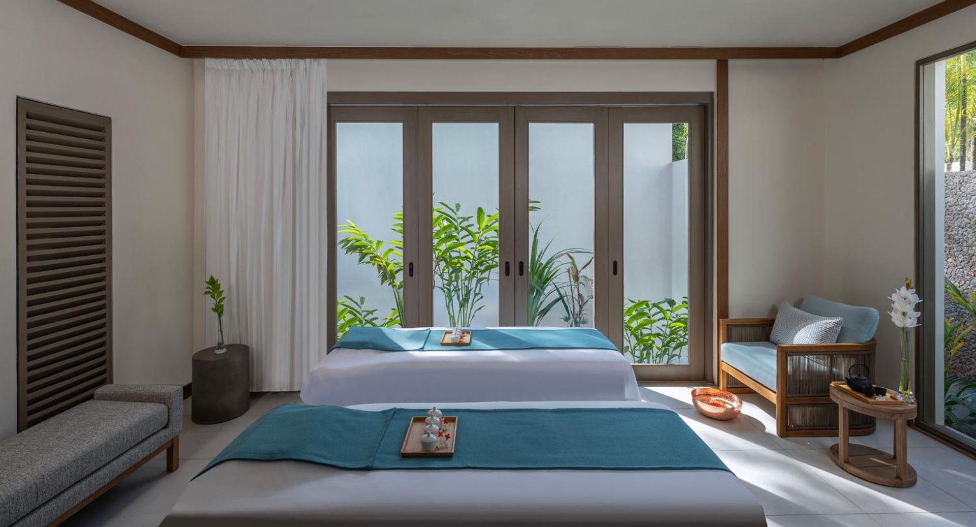 Avani+ Barbarons Seychelles Resort spa procedūru numurs Seišelu salās ar divām kušetēm, gaišu interjeru un skatu uz tropu dārzu