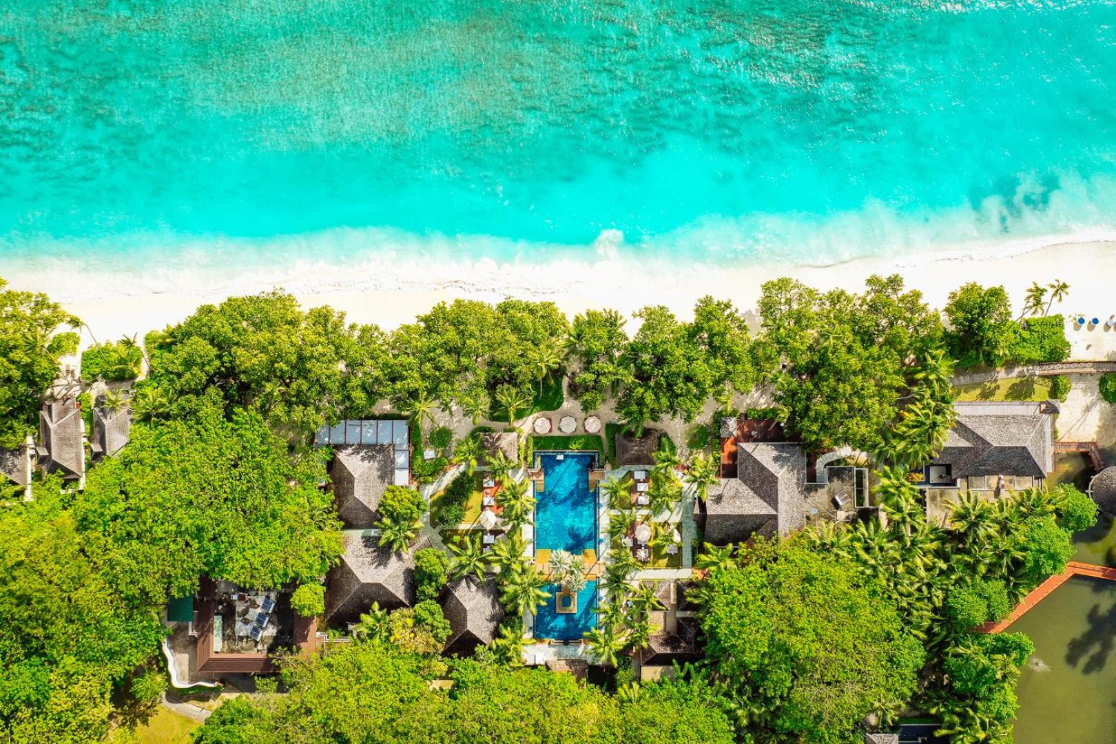 NIVA Labriz Seychelles kūrorta centrālais baseins un bungalo komplekss no augšas, ko ieskauj palmas un balto smilšu pludmale