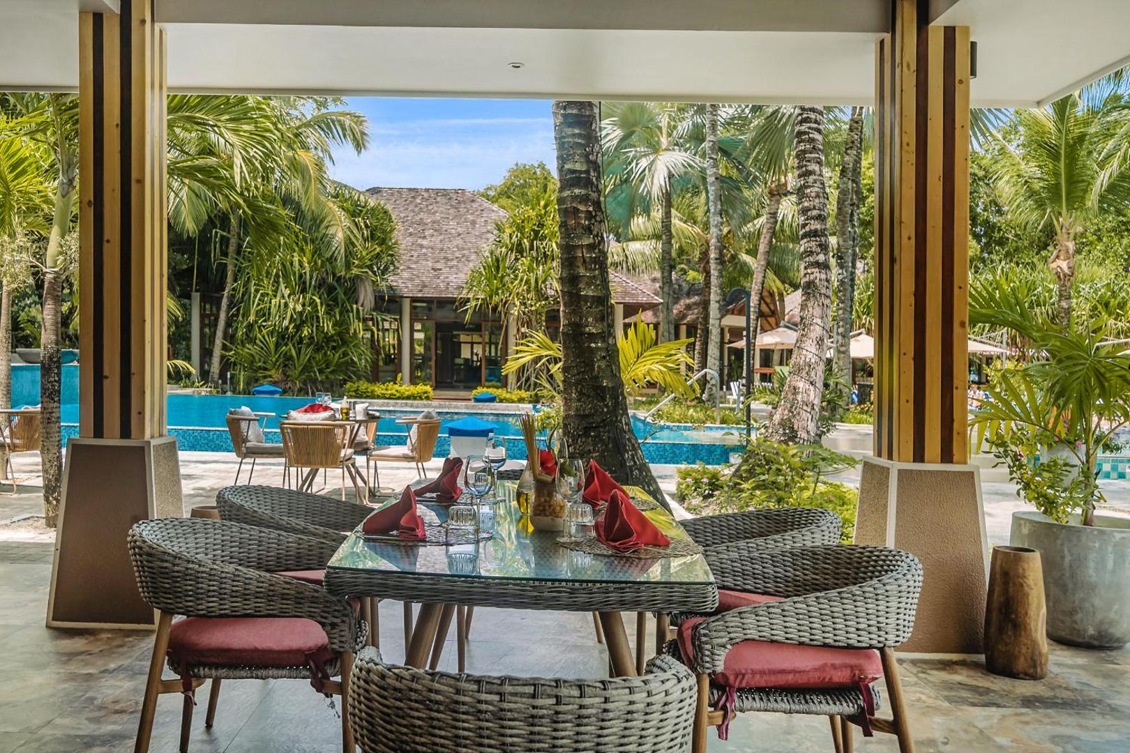 NIVA Labriz Seychelles āra terases restorāns ar klātiem galdiem un skatu uz baseinu un palmu dārzu