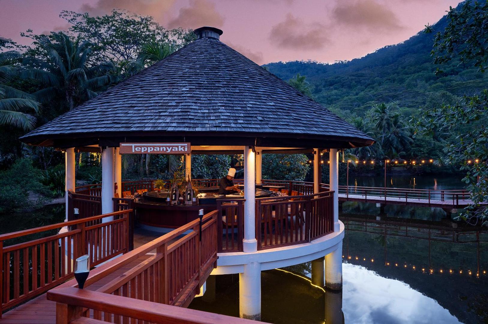 NIVA Labriz Seychelles Teppanyaki restorāns koka lapenē virs ūdens saulrieta laikā ar skatu uz kalniem