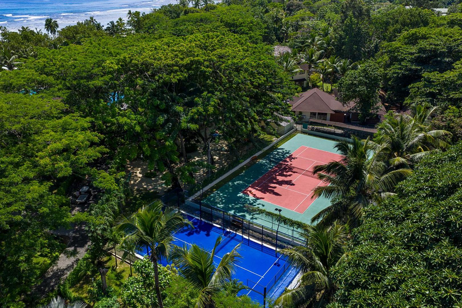 NIVA Labriz Seychelles tenisa un padela korti no putna lidojuma — sporta laukumi ieskauti blīvā tropu mežā pie okeāna krasta