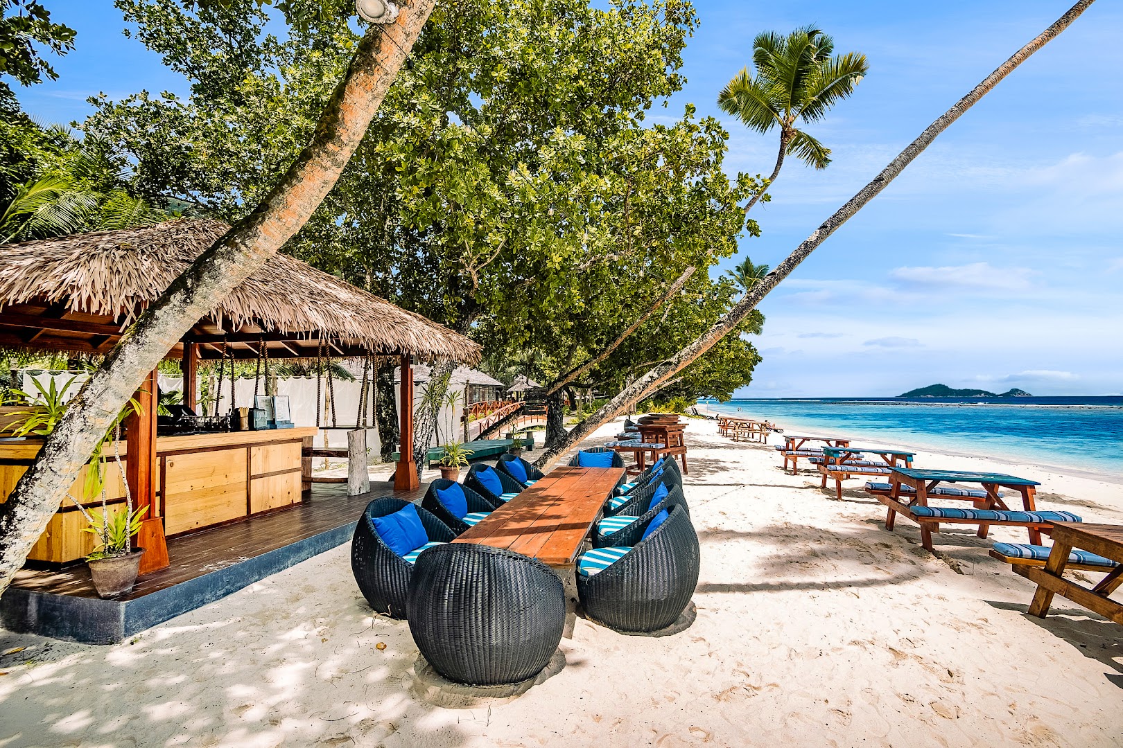 NIVA Labriz Seychelles atpūtas vieta pludmalē ar koka galdiem, zilām mēbelēm un bāru tropu dārza ielokā
