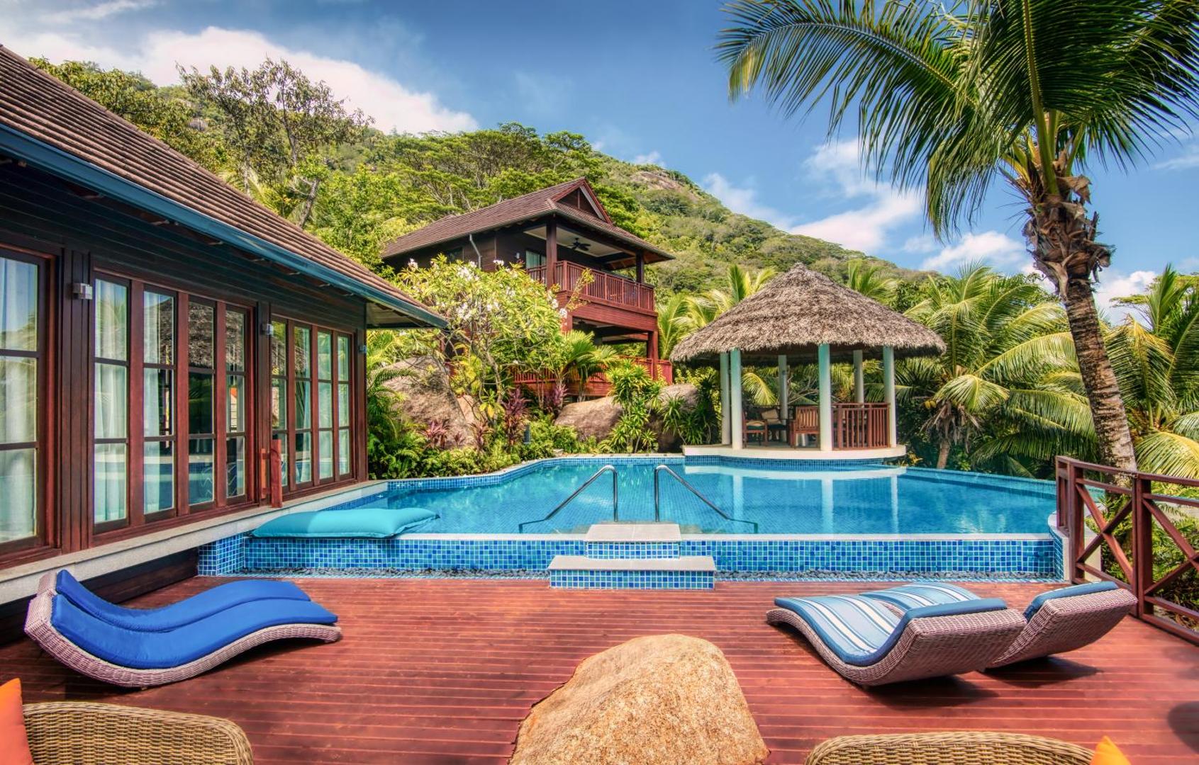NIVA Labriz Seychelles koka villas eksterjers ar privātu baseinu, ziliem sauļošanās krēsliem un lapeni uz kalnu fona