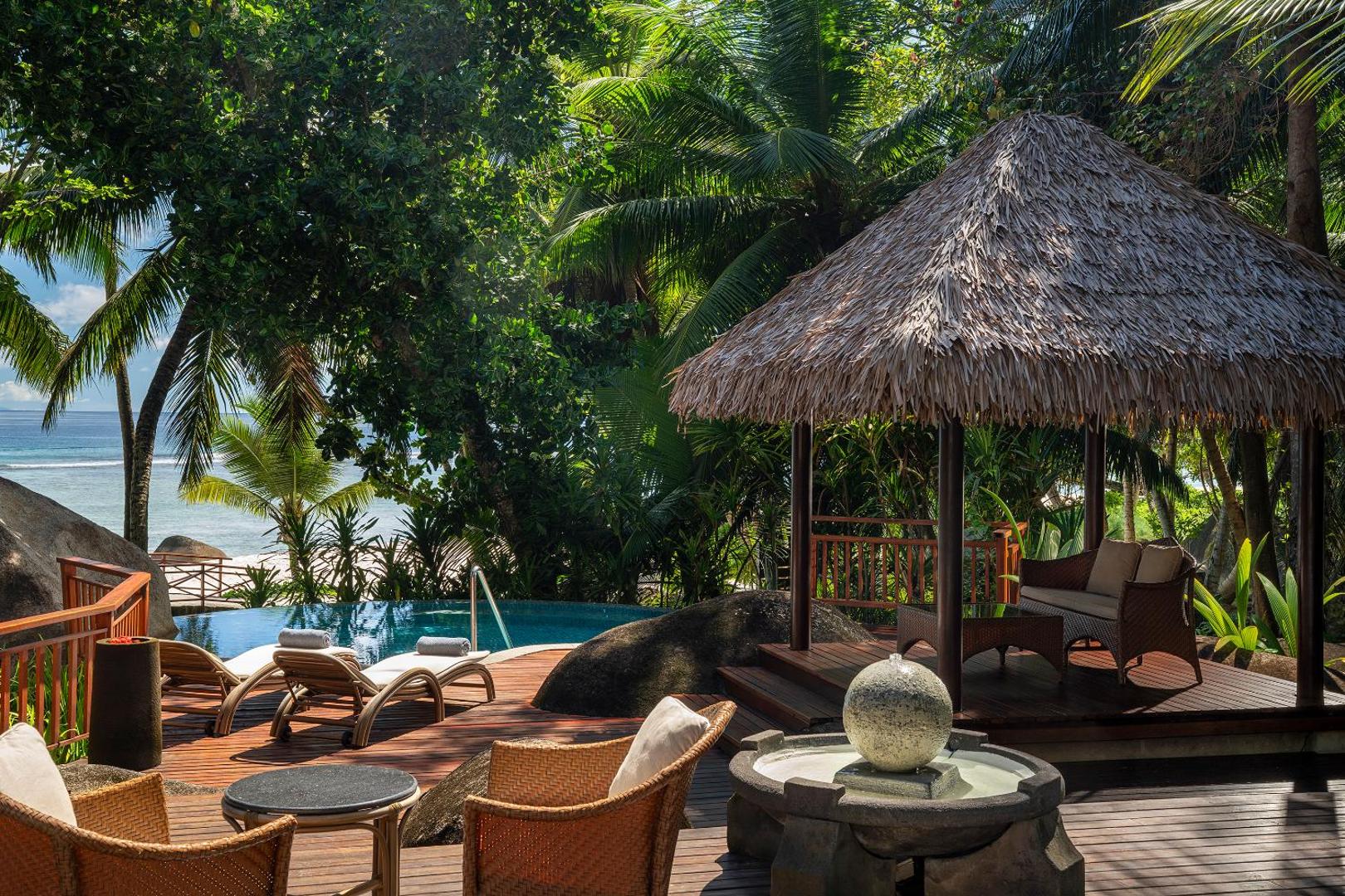 NIVA Labriz Seychelles atpūtas terase ar pītiem krēsliem, dekoratīvu strūklaku un lapeni ar skatu uz tropu dārzu un okeānu