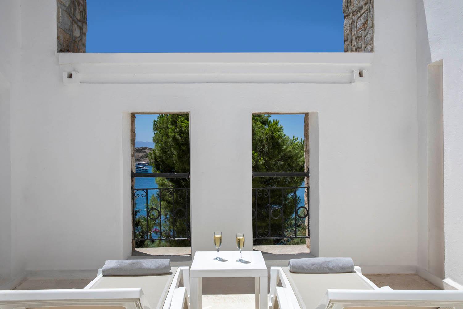 Baska Resort Bodrum terase ar diviem sauļošanās krēsliem, vīna glāzēm un skatu uz jūru caur arkas logiem Bodrumā