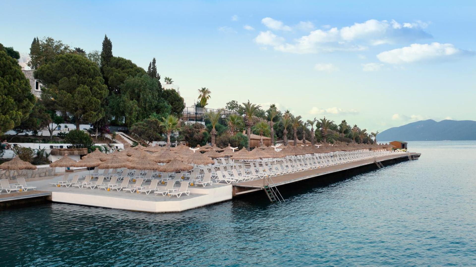 Baska Resort Bodrum plašā koka sauļošanās platforma pie jūras ar daudziem saulessargiem un zviļņiem Bodrumas piekrastē