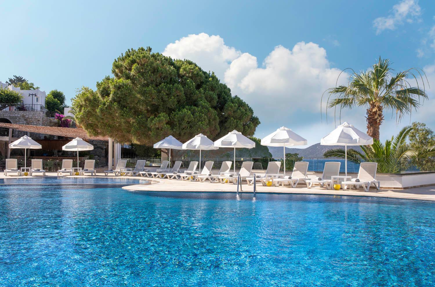 Baska Resort Bodrum āra baseins ar ziliem mozaīkas flīžu rakstiem, saulessargiem un atpūtas krēsliem piekrastē, Bodrumas reģionā, Turcijā.