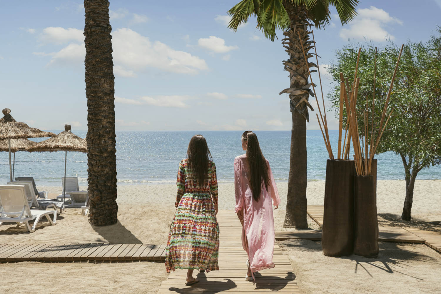 Baska Resort Bodrum pludmales zona ar saulessargiem, palmām un koka dēļu celiņu, kas ved uz jūras krastu