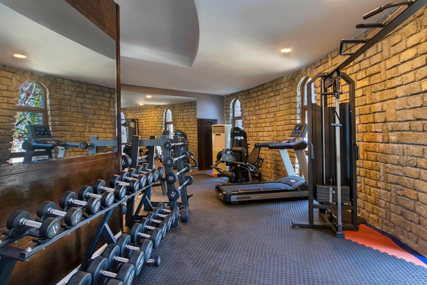 Baska Resort Bodrum fitness centrs ar hantelēm, skrejceliņu un svaru stieņiem telpā ar akmens mūra sienām