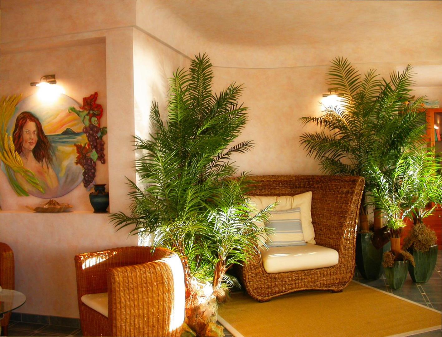 Tonicello Resort & Spa atpūtas stūrītis ar pītiem krēsliem, dekoratīvām palmām un mākslas darbu pie sienas Kalabrijā, Itālijā