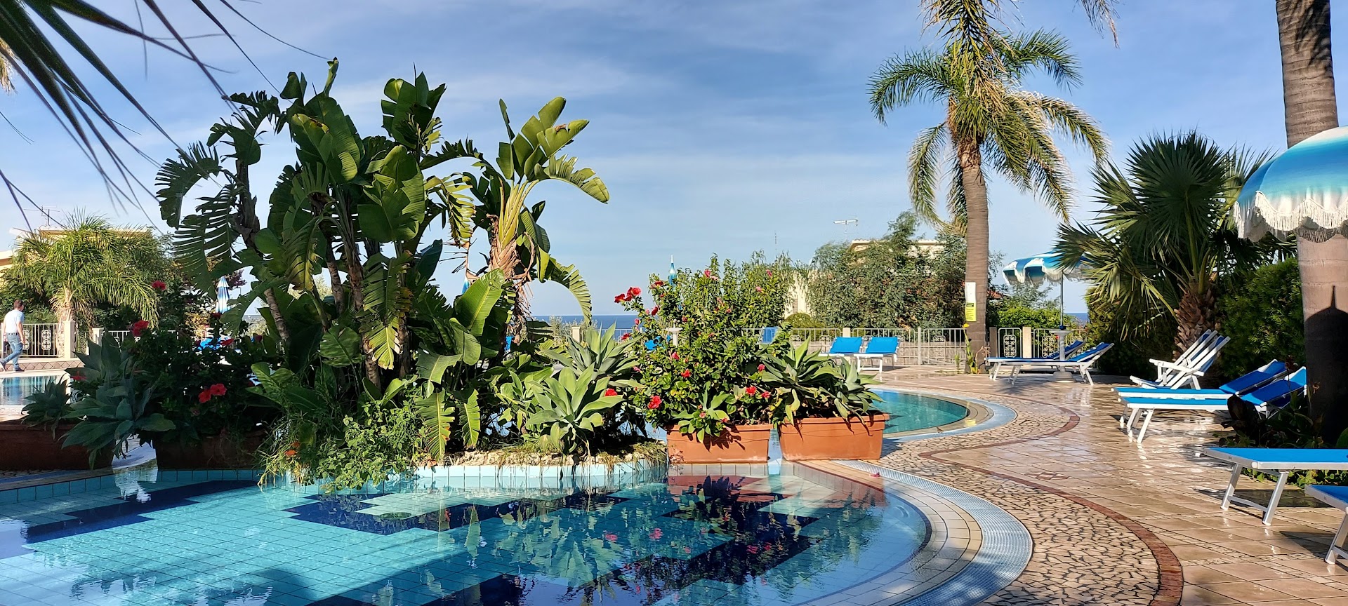 Tonicello Resort & Spa baseina mala ar eksotiskiem augiem, ziediem un atpūtas krēsliem dienas gaismā