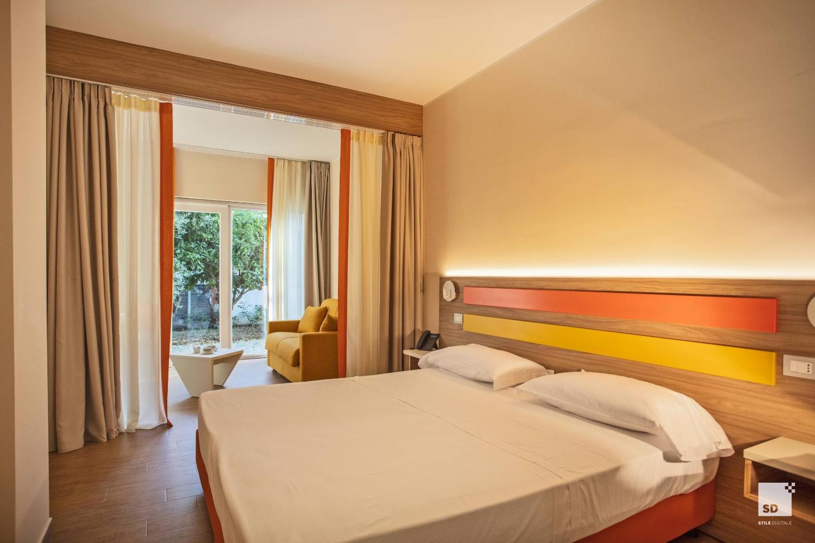 Tonicello Resort & Spa gaišs numurs ar divguļamo gultu un dzeltenu dīvānu atpūtas zonā Kalabrijā, Itālijā — skats uz dārzu