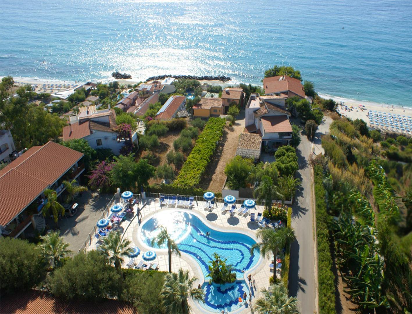 Tonicello Resort & Spa āra baseins ar sauļošanās krēsliem un saulessargiem, ko ieskauj zaļojošs dārzs un skats uz jūru.