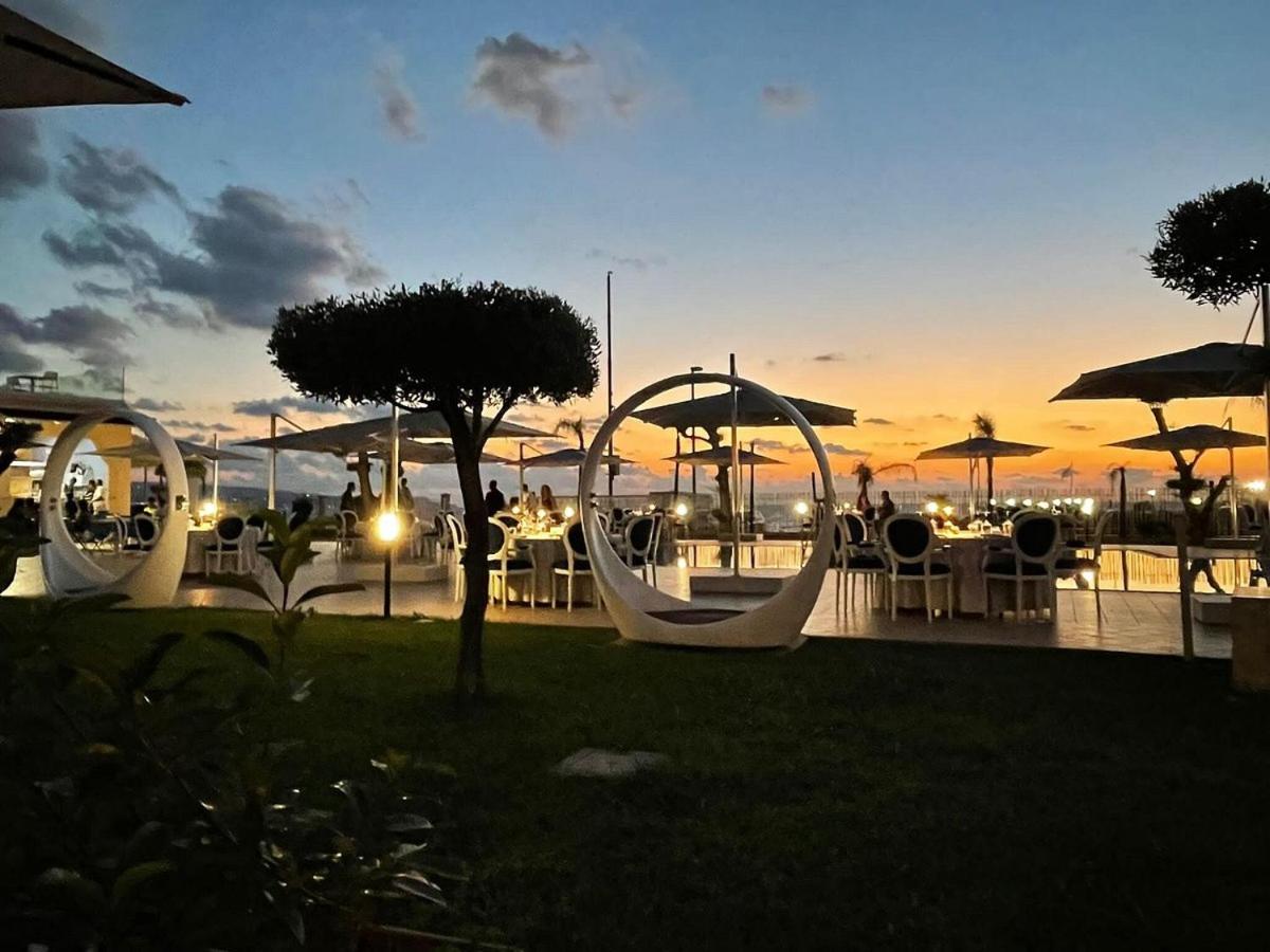 Galia Luxury Resort āra terase saulrieta laikā Kalabrijā ar modernām mēbelēm, dekoratīviem apgaismojuma elementiem un vakariņu galdiem