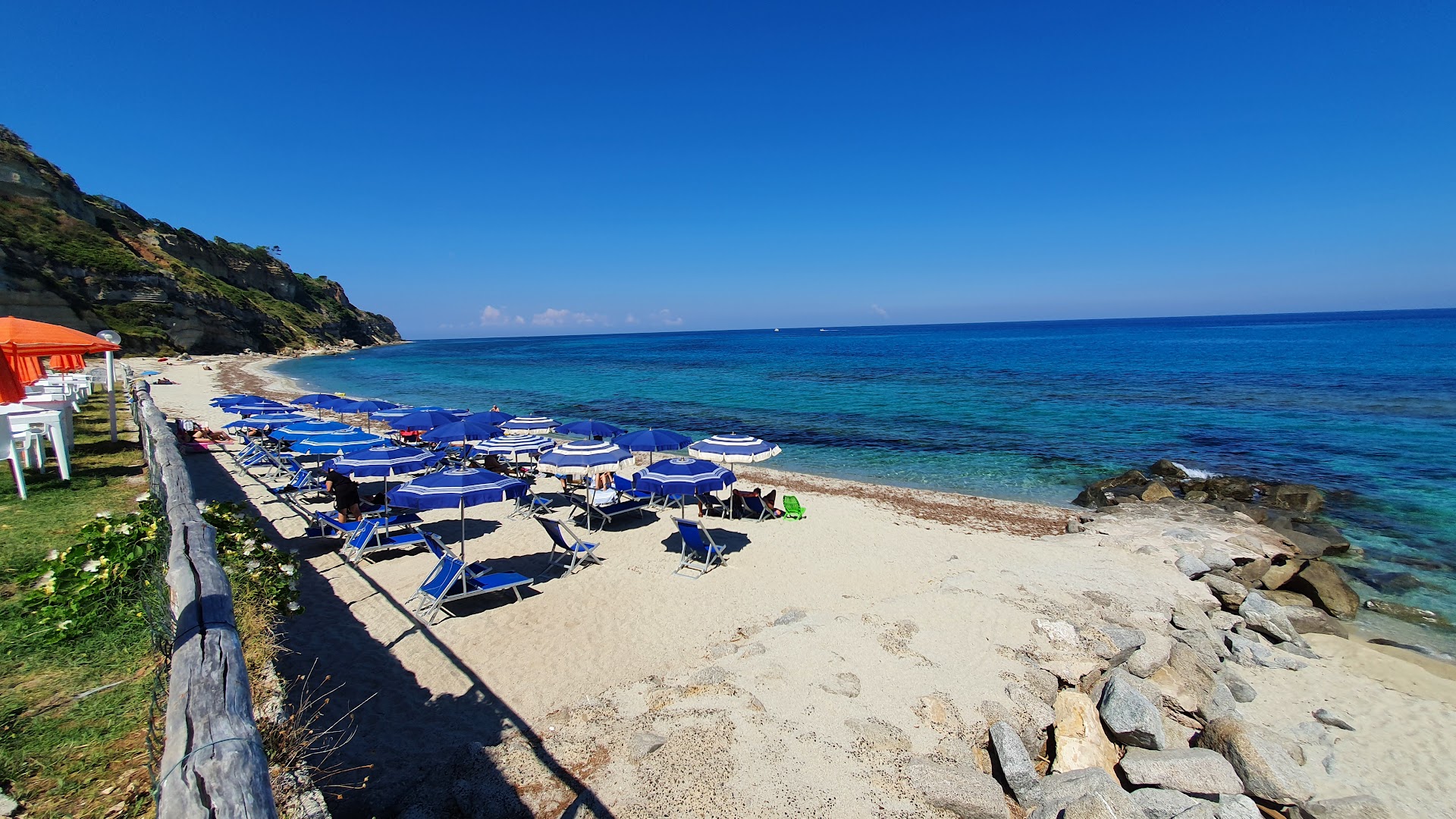 Villagio Marco Polo pludmales zona ar ziliem saulessargiem un sauļošanās krēsliem pie dzidra ūdens Tirēnu jūras piekrastē