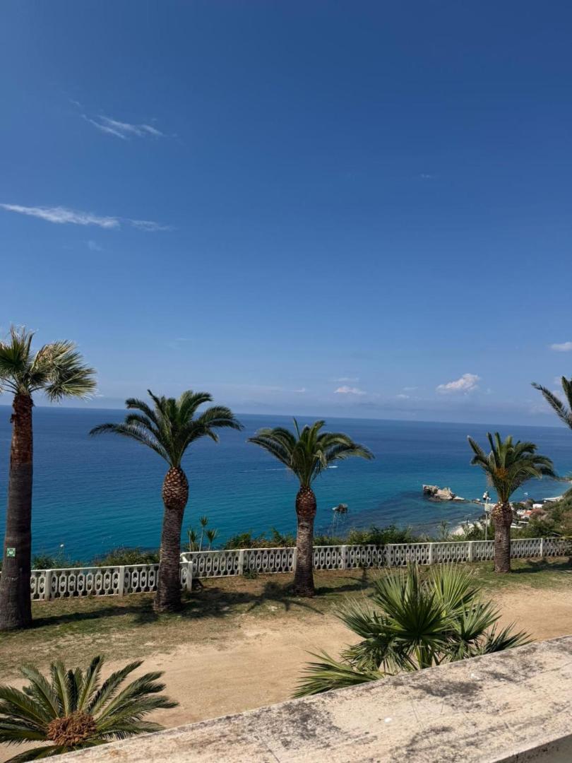 Villagio Marco Polo skats uz Jonijas jūru Kalabrijā caur palmām — zilas debesis un piekrastes panorāma no viesnīcas dārza