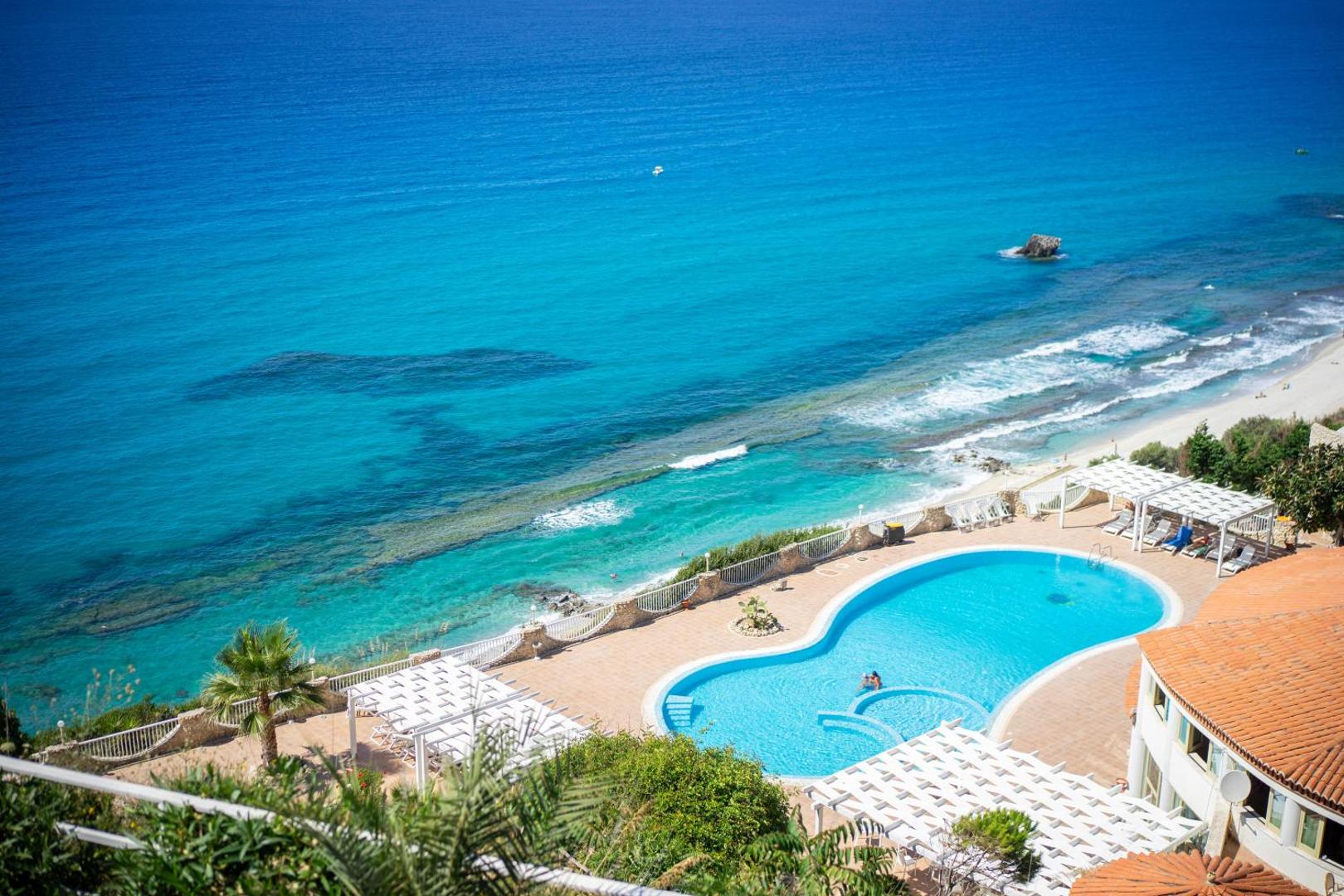 Villagio Marco Polo panorāmas skats no augšas uz baseinu un tirkīzzilo Tirēnu jūru Kalabrijā — pludmale un piekrastes ainava