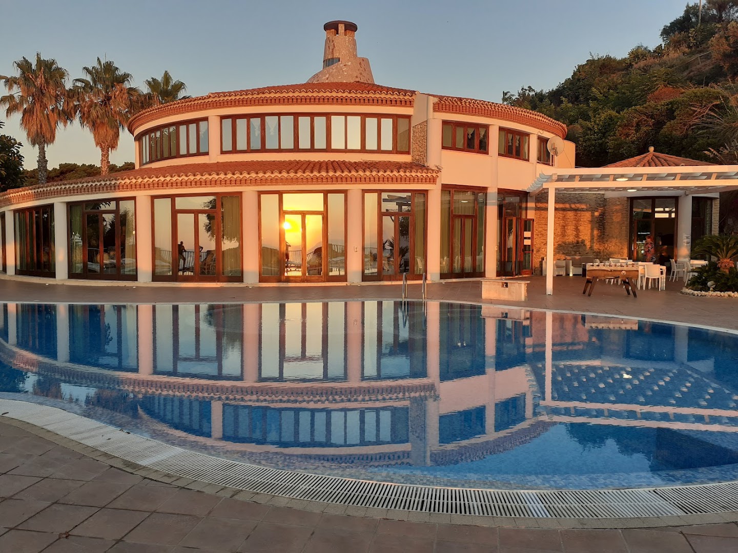 Villagio Marco Polo viesnīcas galvenā ēka un baseins saulrieta laikā Kalabrijā, Itālijā — saules atspulgs logos un mierīgs ūdens
