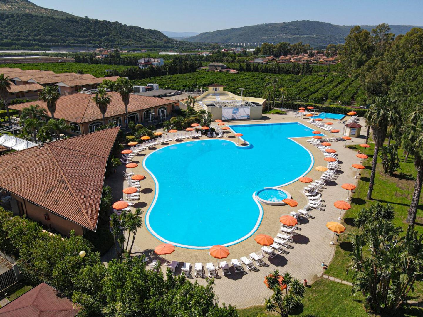 Futura Club La Praya viesnīcas teritorijas panorāma ar lielu baseinu, bungalo tipa ēkām un zaļiem dārziem Kalabrijas kalnu fonā.