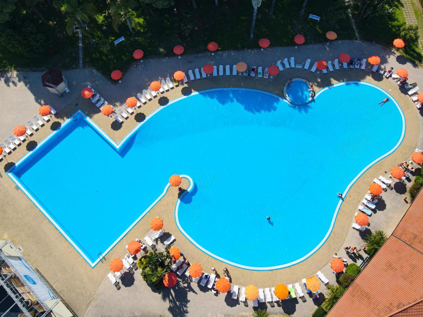 Futura Club La Praya lielais āra baseins no putna lidojuma ar ziliem ūdeņiem, oranžiem saulessargiem un sauļošanās krēsliem.