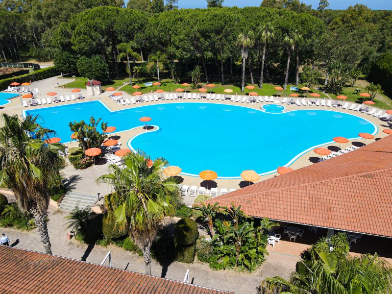 Futura Club La Praya baseina zona ar palmām un sauļošanās krēsliem Kalabrijas reģionā, skats uz viesnīcas centrālo ēku un dārzu.