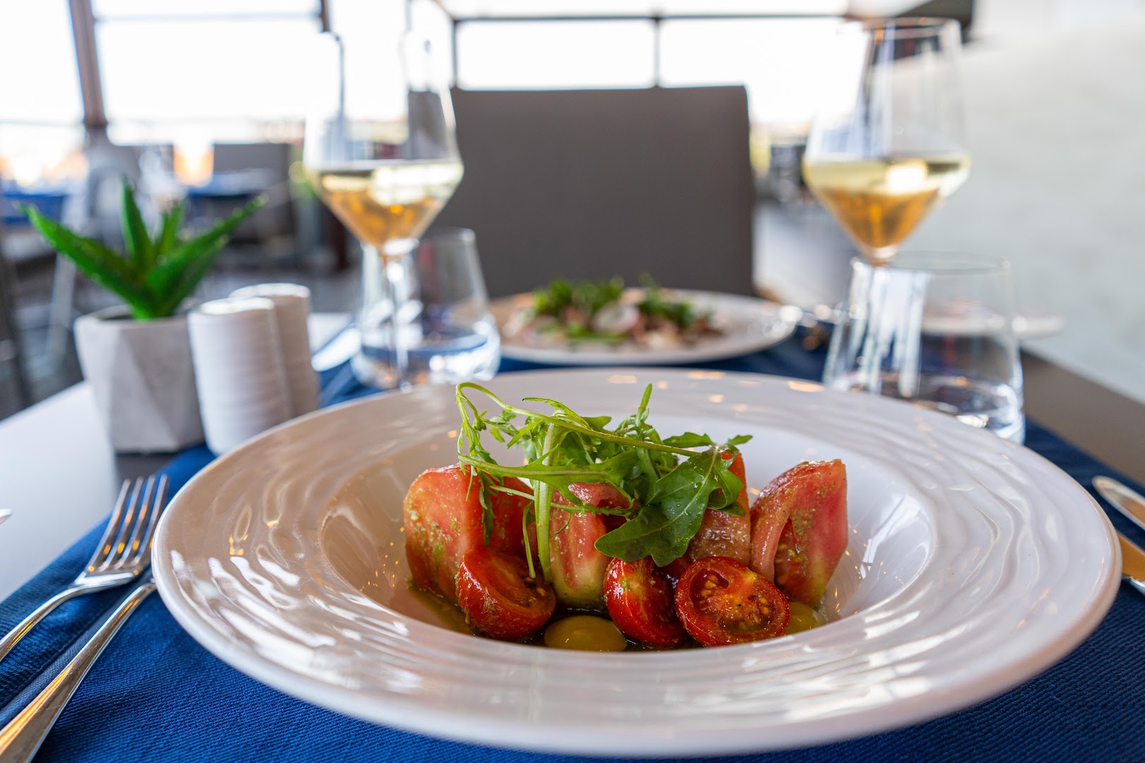 HVD Club Hotel Miramar restorāna servējums ar svaigiem tomātu salātiem un vīna glāzēm uz zila galdauta