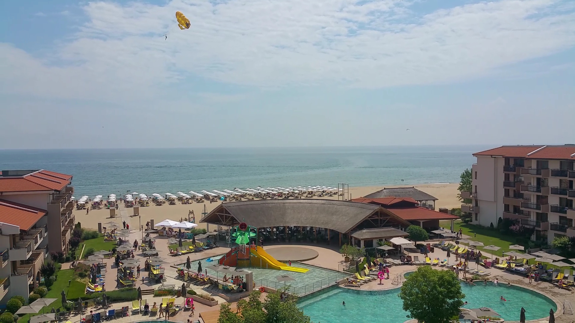 HVD Club Hotel Miramar Obzorā — skats no augšas uz baseinu zonu, bērnu ūdens slidkalniņiem un plašo smilšu pludmali Melnās jūras krastā.