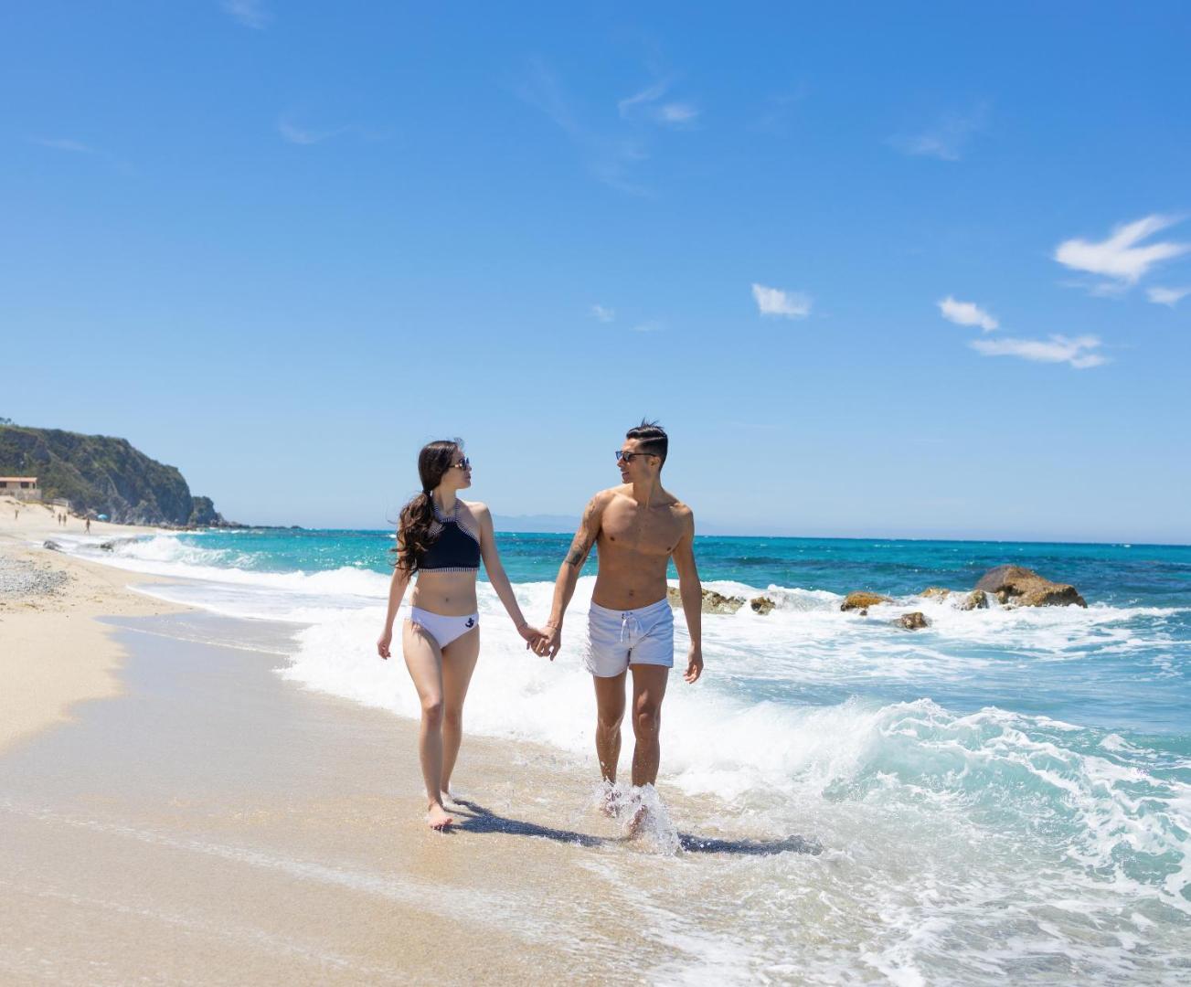 Pāris pastaigājas pa Midenza Seaside & Nature Retreat smilšu pludmali gar jūras krastu saulainā laikā Kalabrijā