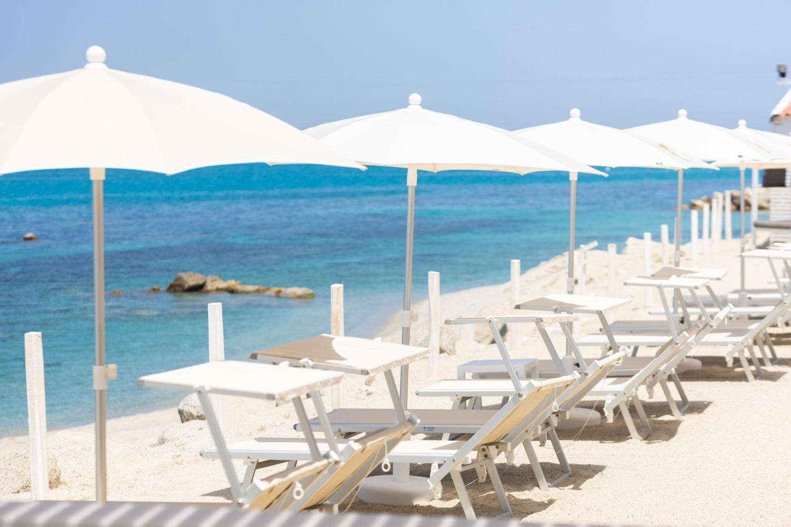 Midenza Seaside & Nature Retreat pludmales zona ar baltiem saulessargiem un zviļņiem pie zilas jūras saulainā dienā Itālijā
