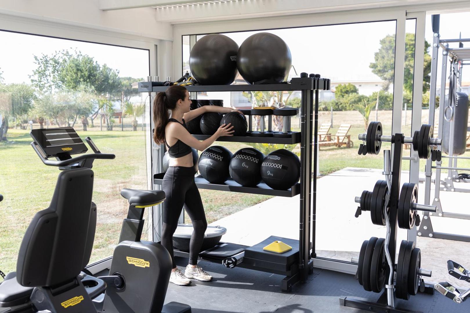 Midenza Seaside & Nature Retreat moderns fitness centrs ar Technogym aprīkojumu, svariem un lieliem logiem uz dārzu
