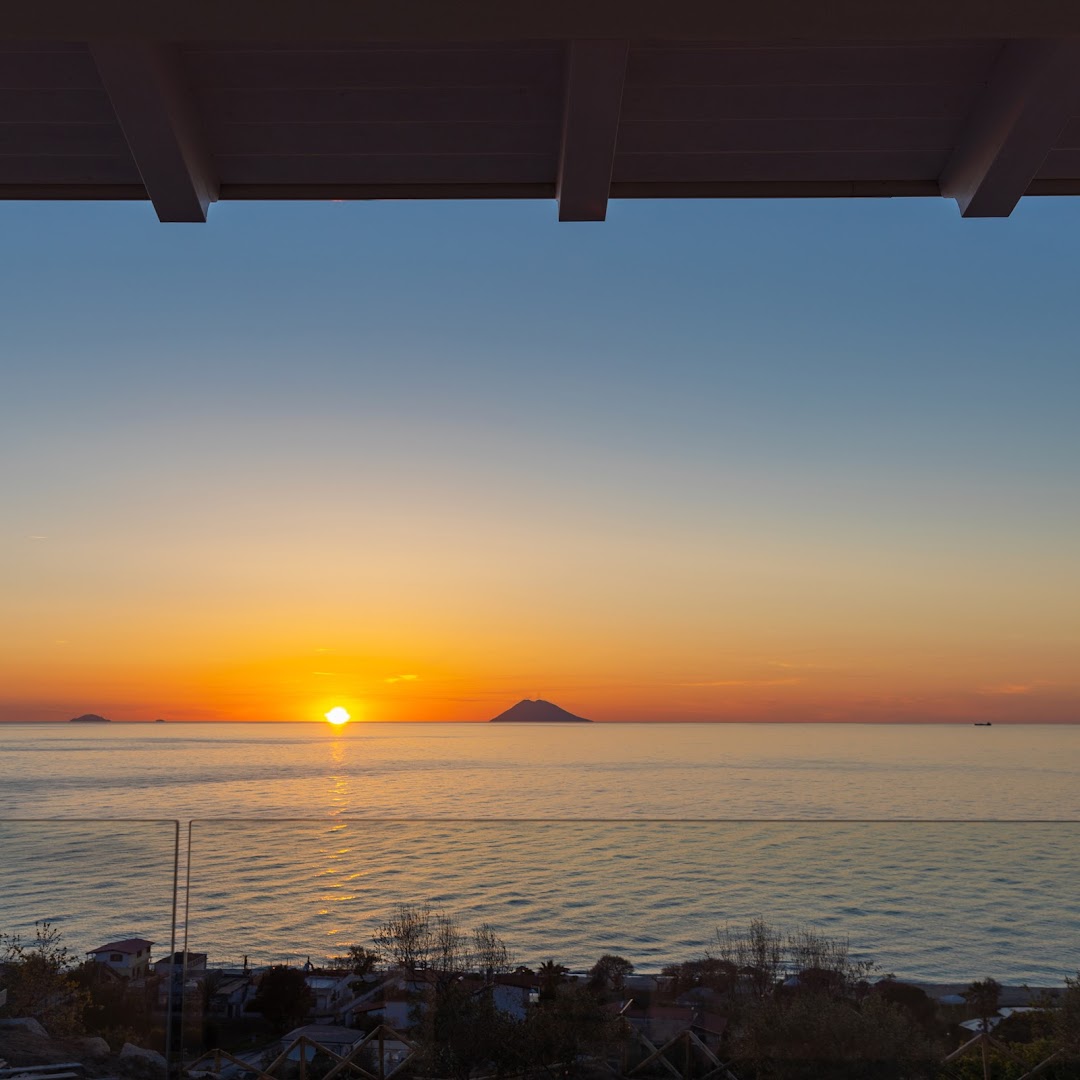 Saulriets virs Tirēnu jūras, skatoties no Midenza Seaside & Nature Retreat terases, ar skatu uz Stromboli vulkāna siluetu.