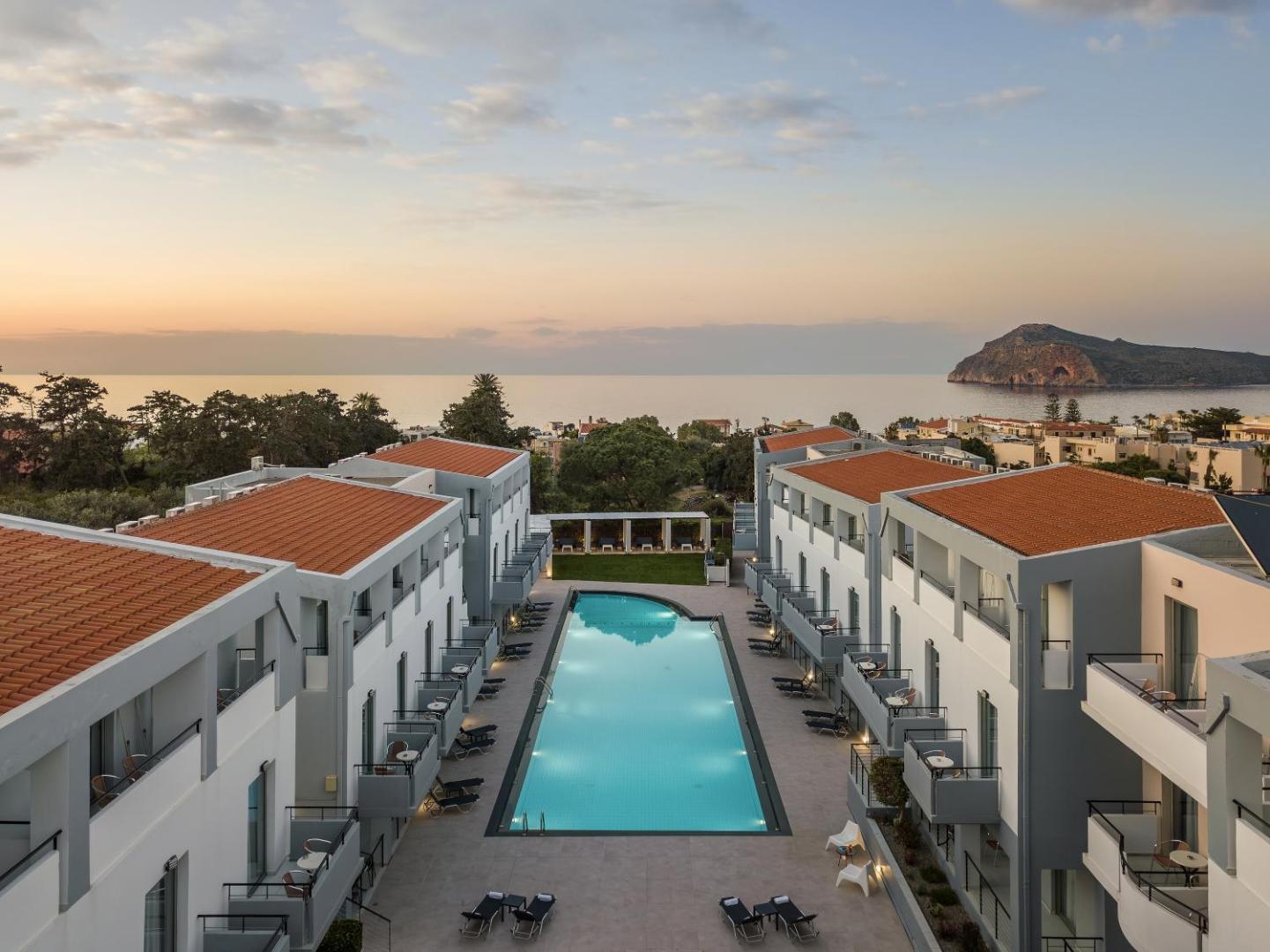 Sunrise Village Hotel skats no augšas uz āra baseinu un numuru korpusiem saulrietā ar skatu uz jūru un salu