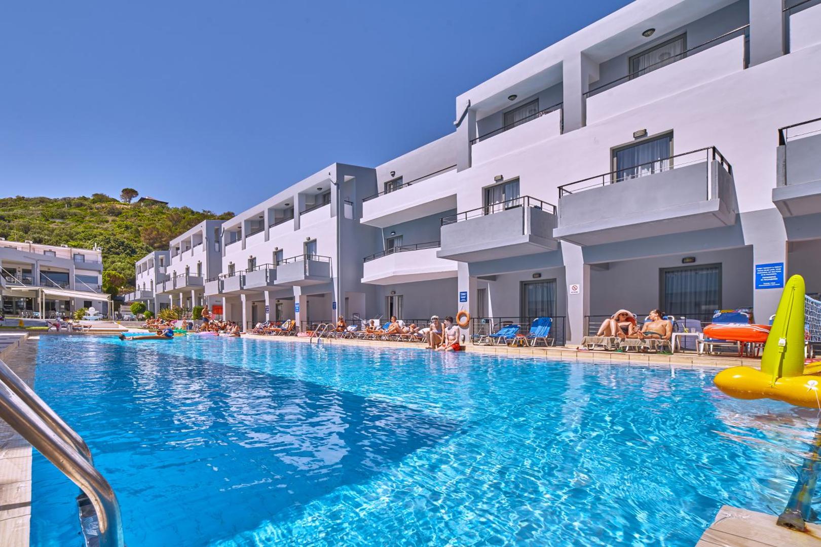 Sunrise Village Hotel plašais āra baseins dienas laikā ar atpūtniekiem un saulessargiem pie viesnīcas numuriem