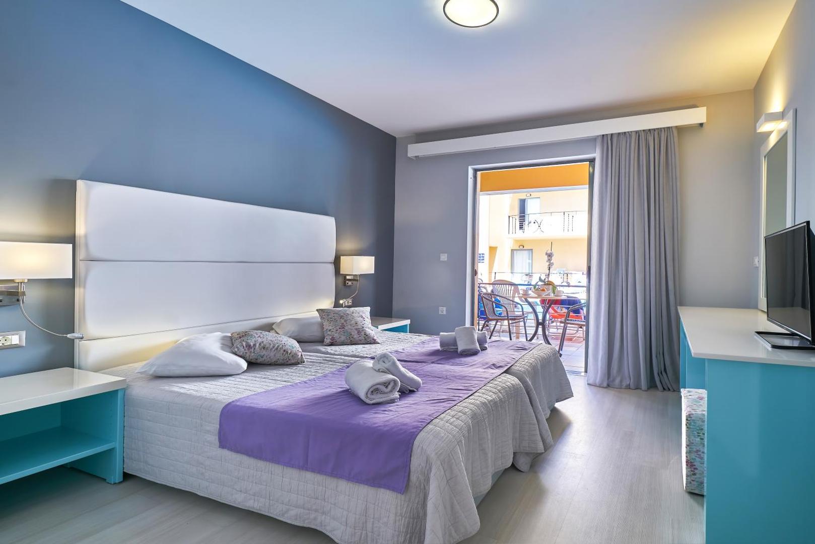 Sunrise Village Hotel numurs ar divām gultām, ziliem akcentiem un izeju uz mēbelētu balkonu, kas vērsts pret iekšpagalmu
