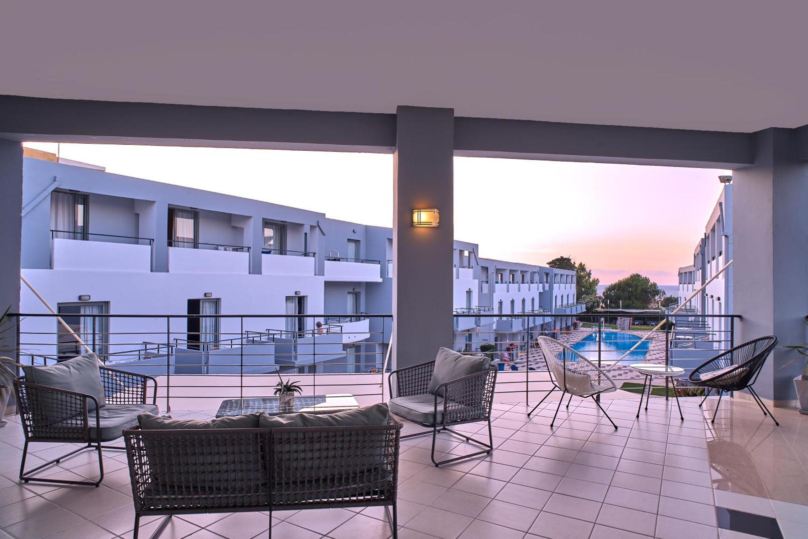 Sunrise Village Hotel koplietošanas terase ar modernām mēbelēm un skatu uz āra baseinu un viesnīcas korpusiem saulrietā