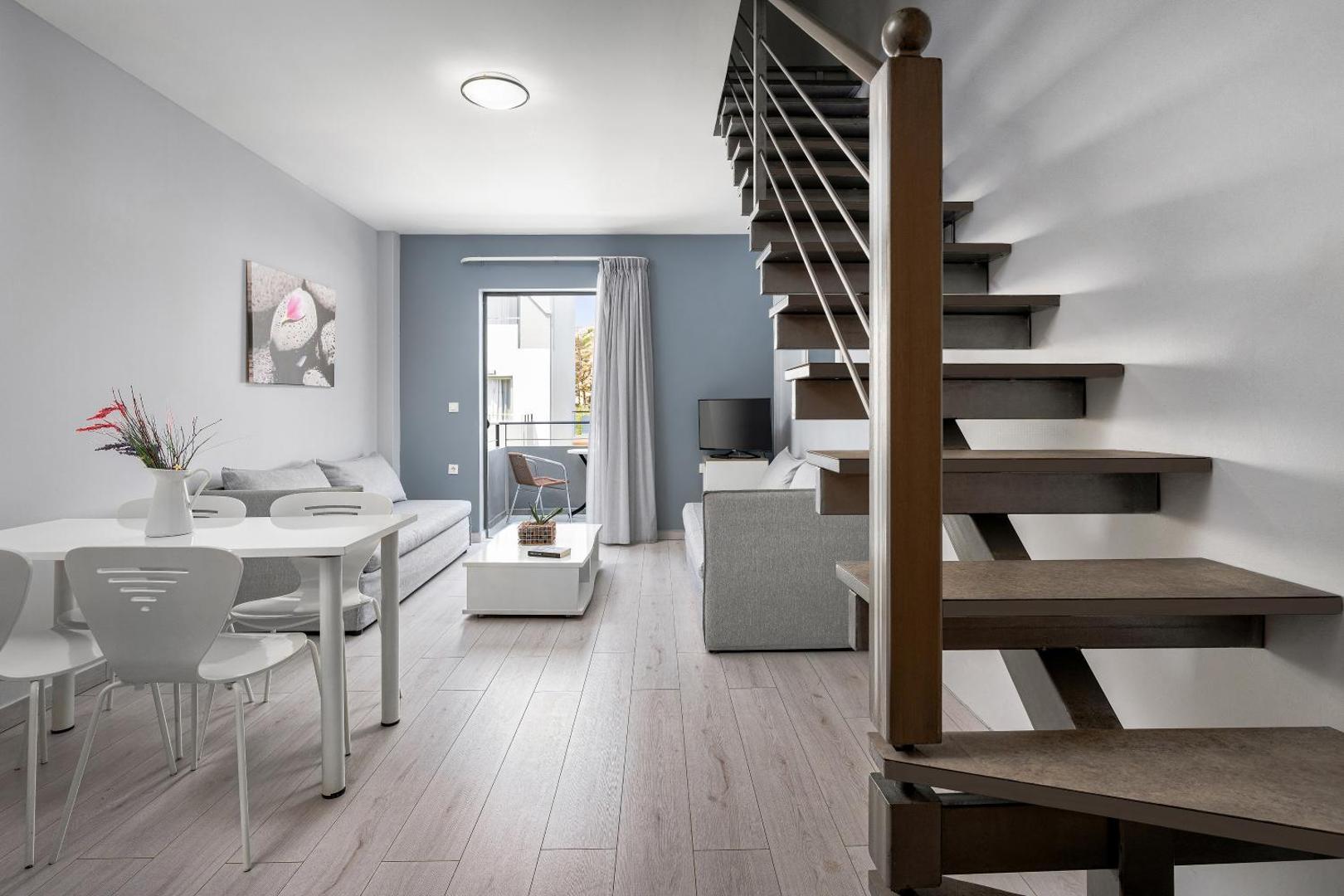 Sunrise Village Hotel divstāvu apartamenti ar koka kāpnēm, dzīvojamo zonu, dīvānu un ēdamgaldu gaišā, modernā stilā