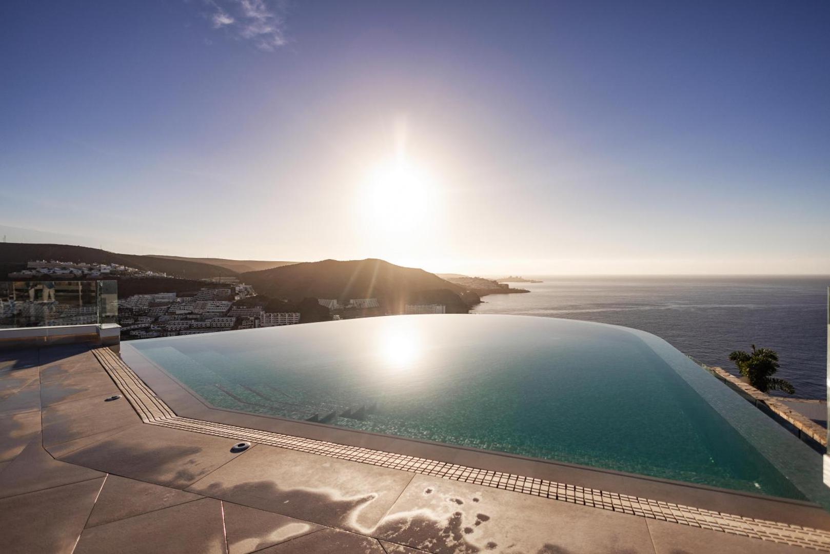Servatur Puerto Azul Hotel bezgalības baseins ar skatu uz okeānu Grankanārijā — saules gaisma atspīd ūdenī virs piekrastes klintīm
