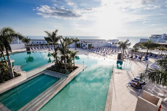 Servatur Puerto Azul Hotel plašā baseinu zona ar skatu uz jūru Grankanārijā — vairāki baseini, palmas un sauļošanās krēsli