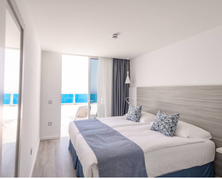 Gaišs Servatur Puerto Azul Hotel numurs ar divguļamo gultu un izeju uz balkonu, no kura paveras skats uz okeānu