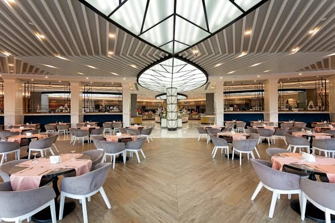 Long Beach Resort galvenais restorāns ar modernu interjeru, gaišām koka grīdām un plašu bufetes zonu fonā Alānijā, Turcijā