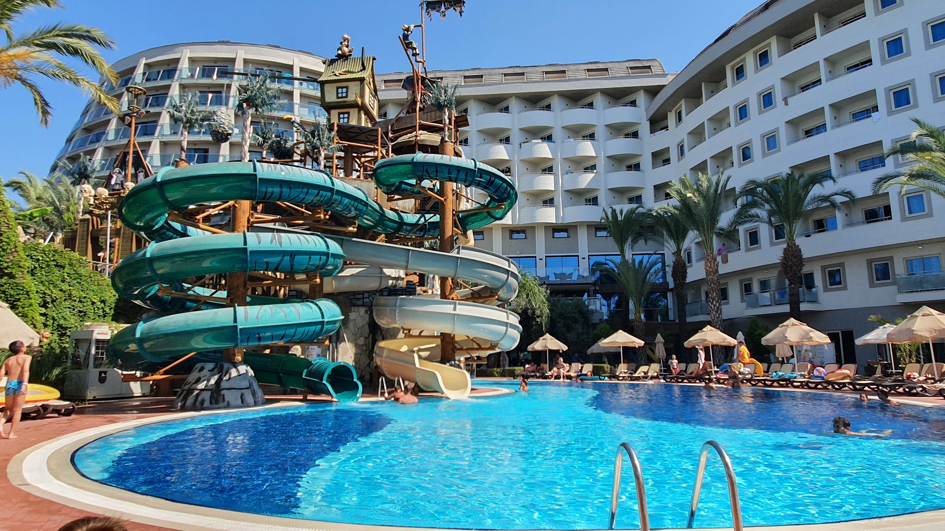 Long Beach Resort ūdens slidkalniņi pie viesnīcas korpusa un baseina zona ar atpūtas krēsliem Turcijā