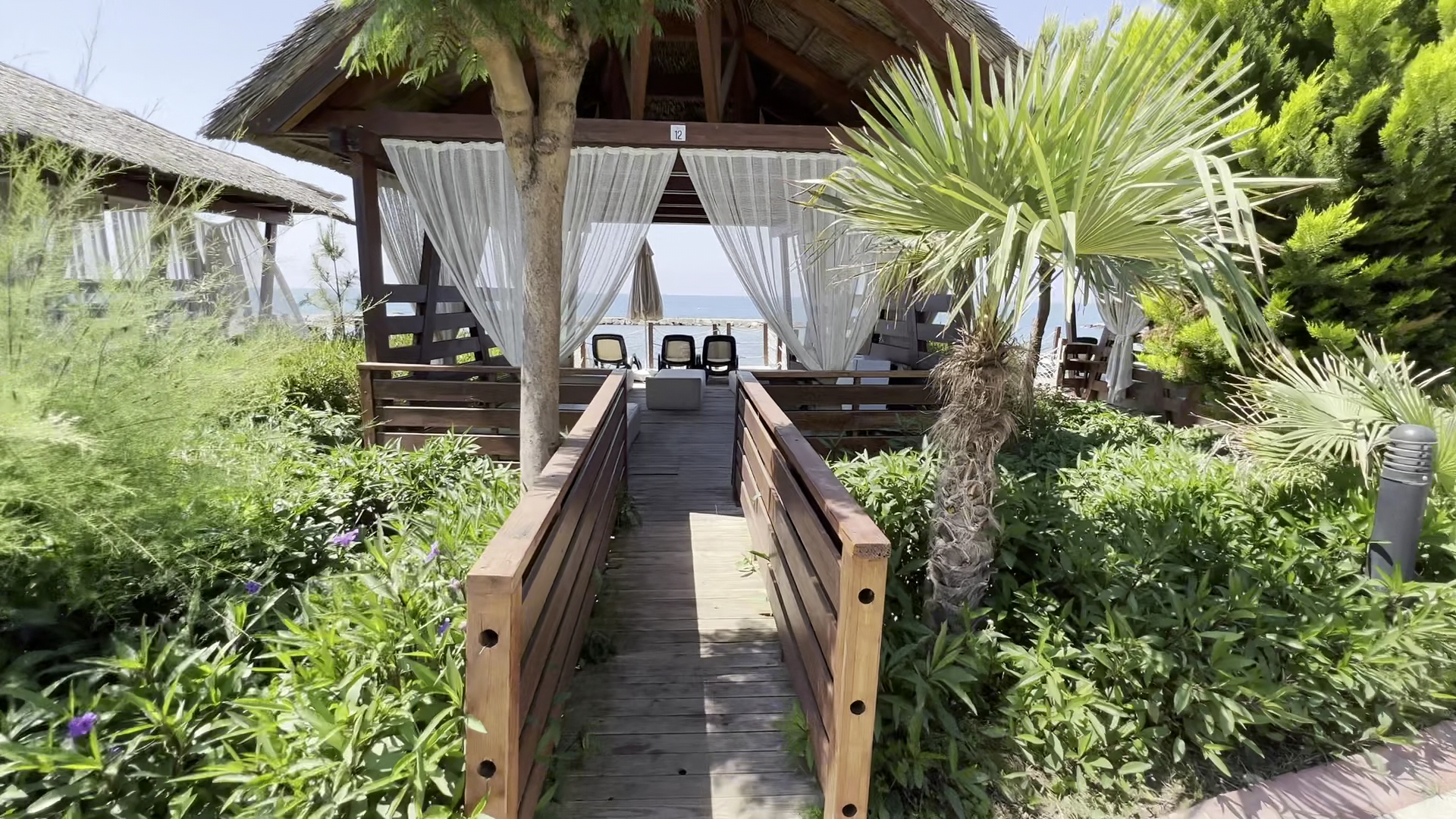 Long Beach Resort privātie pludmales bungalo ar koka terasi, baltiem aizkariem un skatu uz jūru palmu un zaļumu ieskāvumā