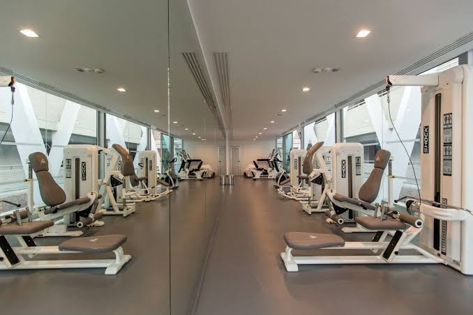 Santa Mónica Suites Hotel moderns fitness centrs ar trenažieriem, lieliem spoguļiem un skatu uz viesnīcas arhitektūru