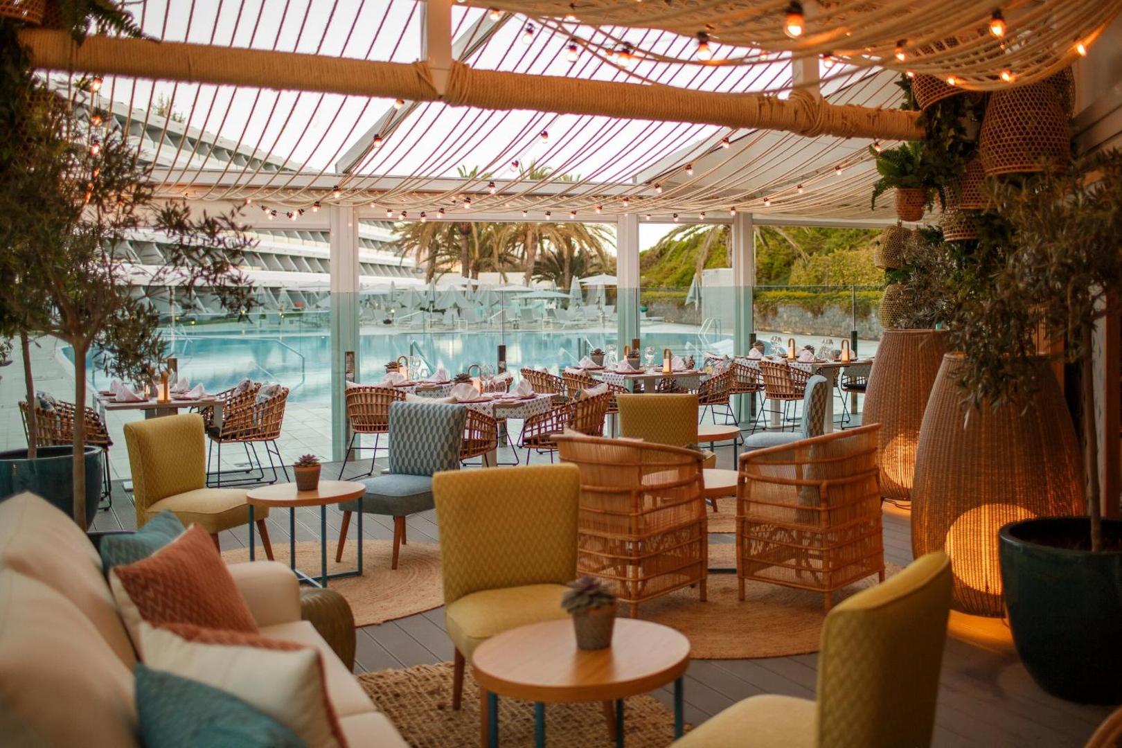 Santa Mónica Suites Hotel restorāna terase ar stilīgām mēbelēm un skatu uz baseinu vakarā — mājīgs apgaismojums un moderna atmosfēra