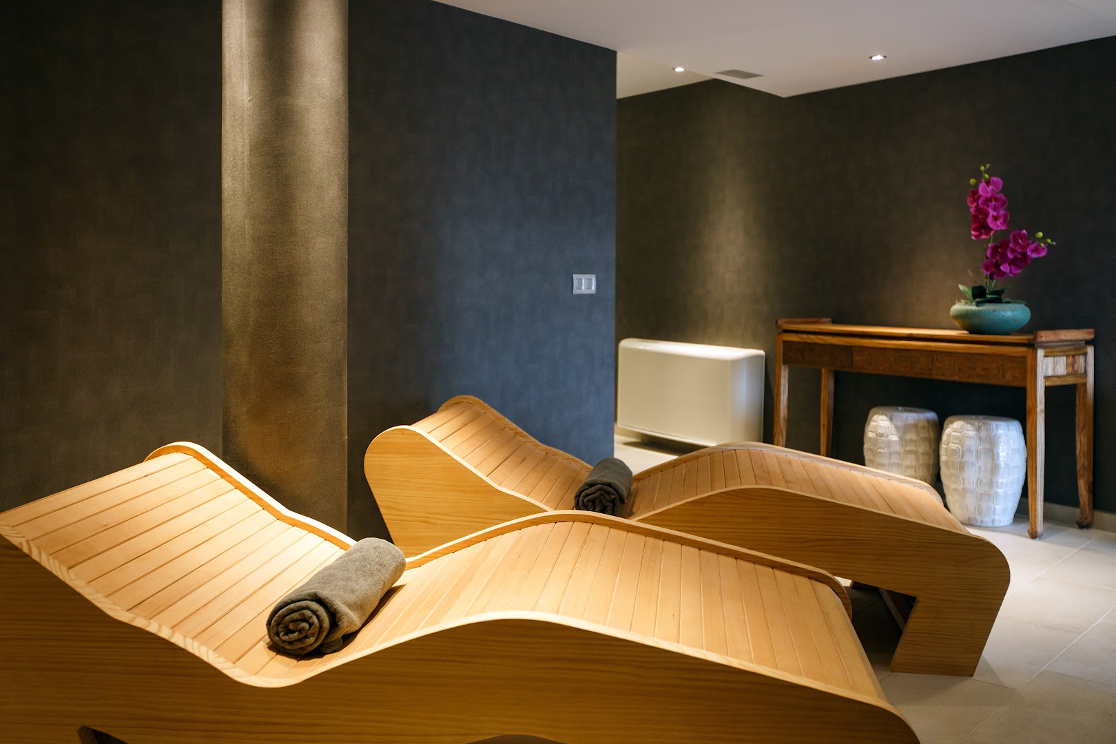 Santa Mónica Suites Hotel spa centra relaksācijas telpa ar koka guļamkrēsliem, tumšām sienām un dekoratīviem ziediem mierīgā gaisotnē