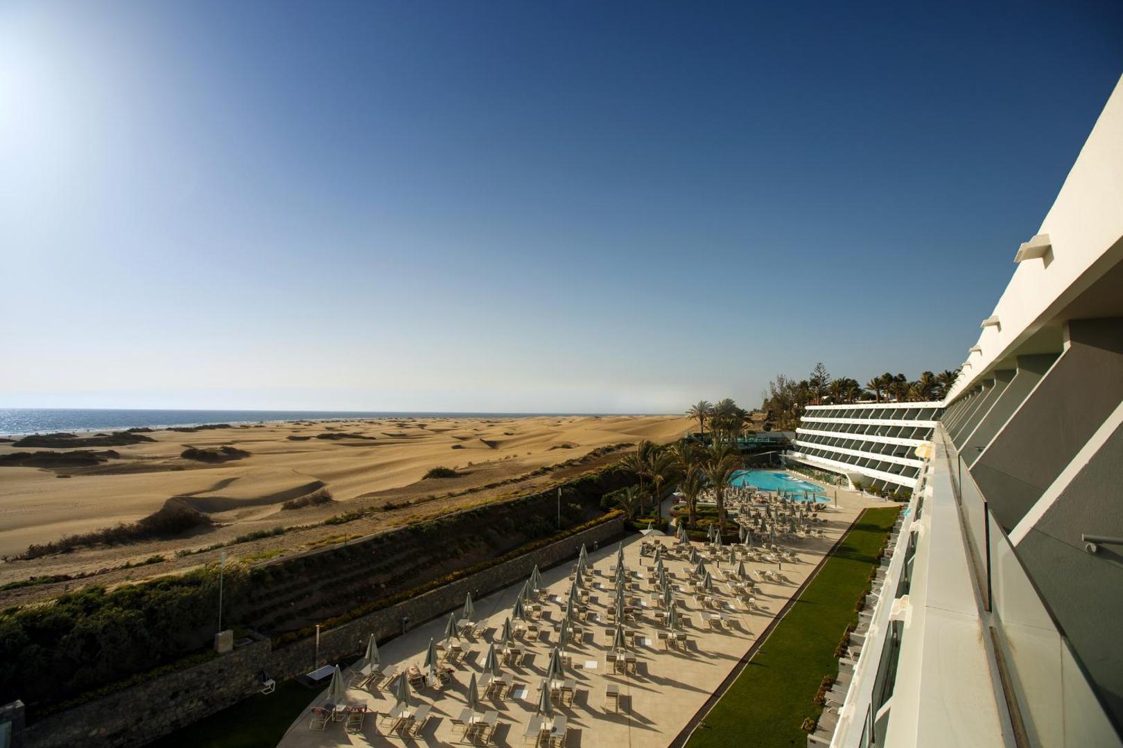Santa Mónica Suites Hotel modernā arhitektūra un numuru balkoni ar skatu uz baseinu un Maspalomas kāpām saulainā dienā