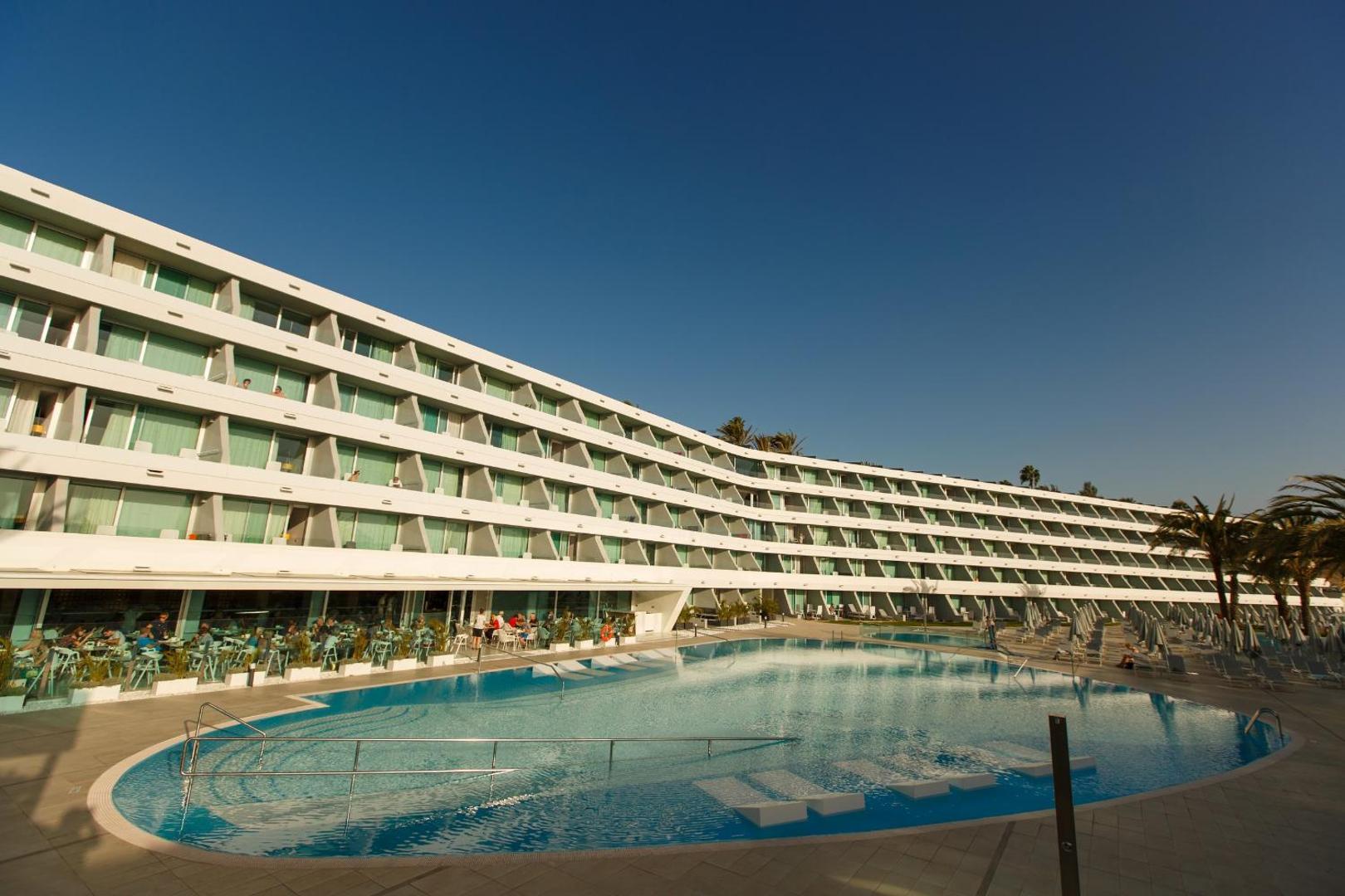 Santa Mónica Suites Hotel modernā fasāde ar balkoniem un plašu āra baseinu zem skaidrām debesīm Grankanārijā