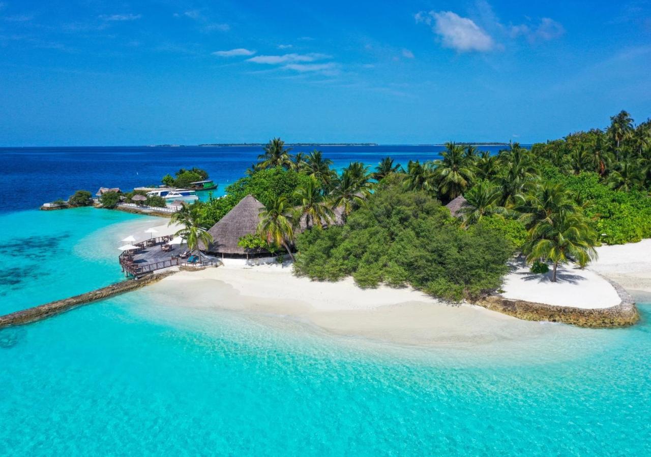 Makunudu Island panorāmas skats uz kūrorta galveno ēku ar salmu jumtu, pludmali un kristāldzidru okeāna ūdeni saulainā dienā