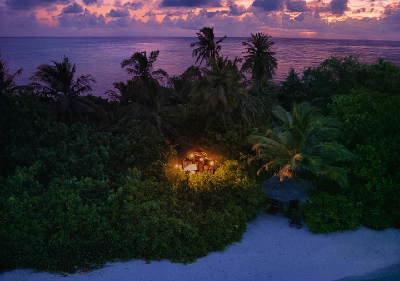 Makunudu Island vakara skats uz izgaismotu bungalo tropu dārzā pie pludmales purpursarkana saulrieta debesīs
